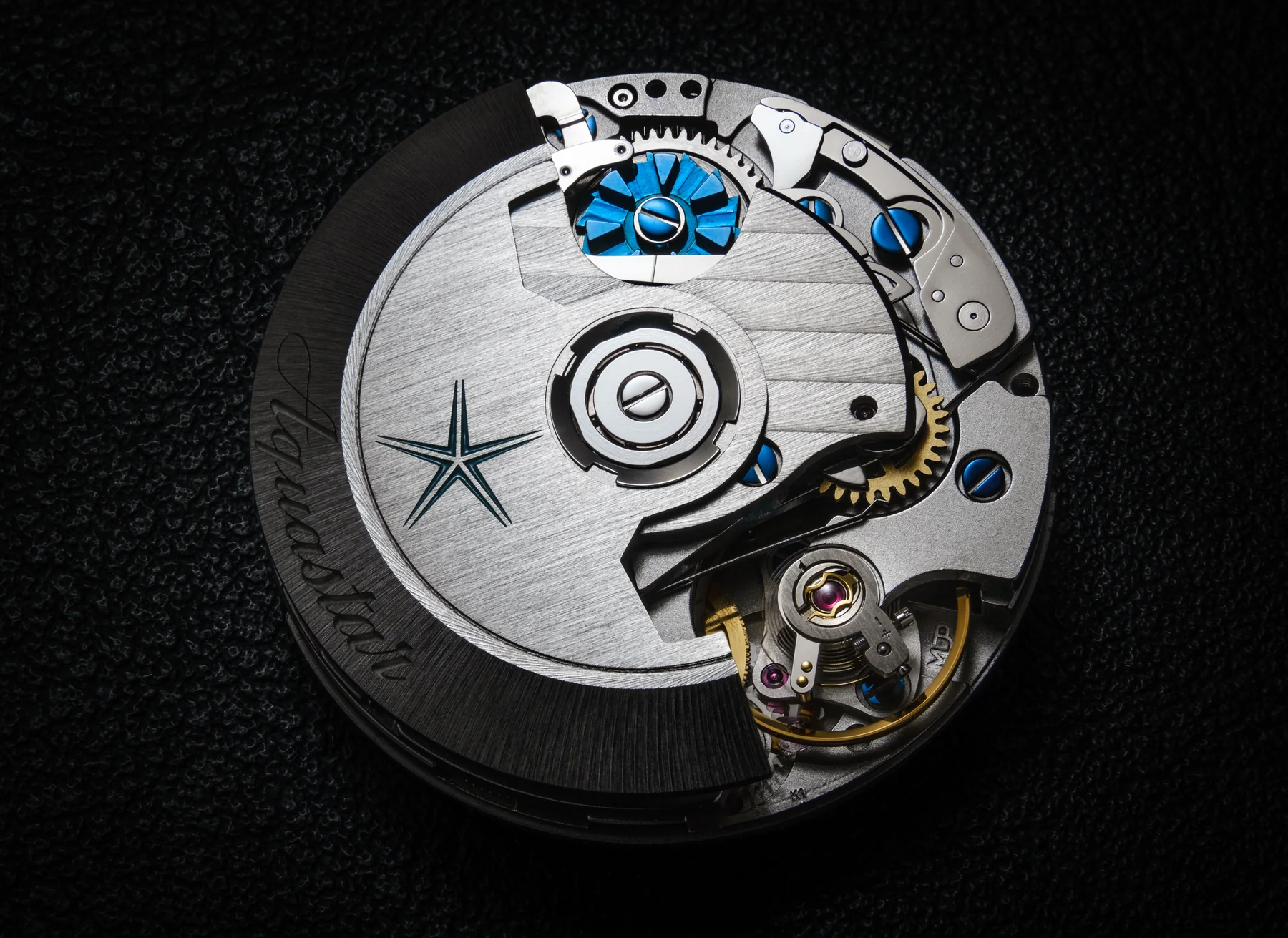 Macro of the Aquastar chronograph movement with the blue column wheel visible at the centre, surrounded by the chronograph levers