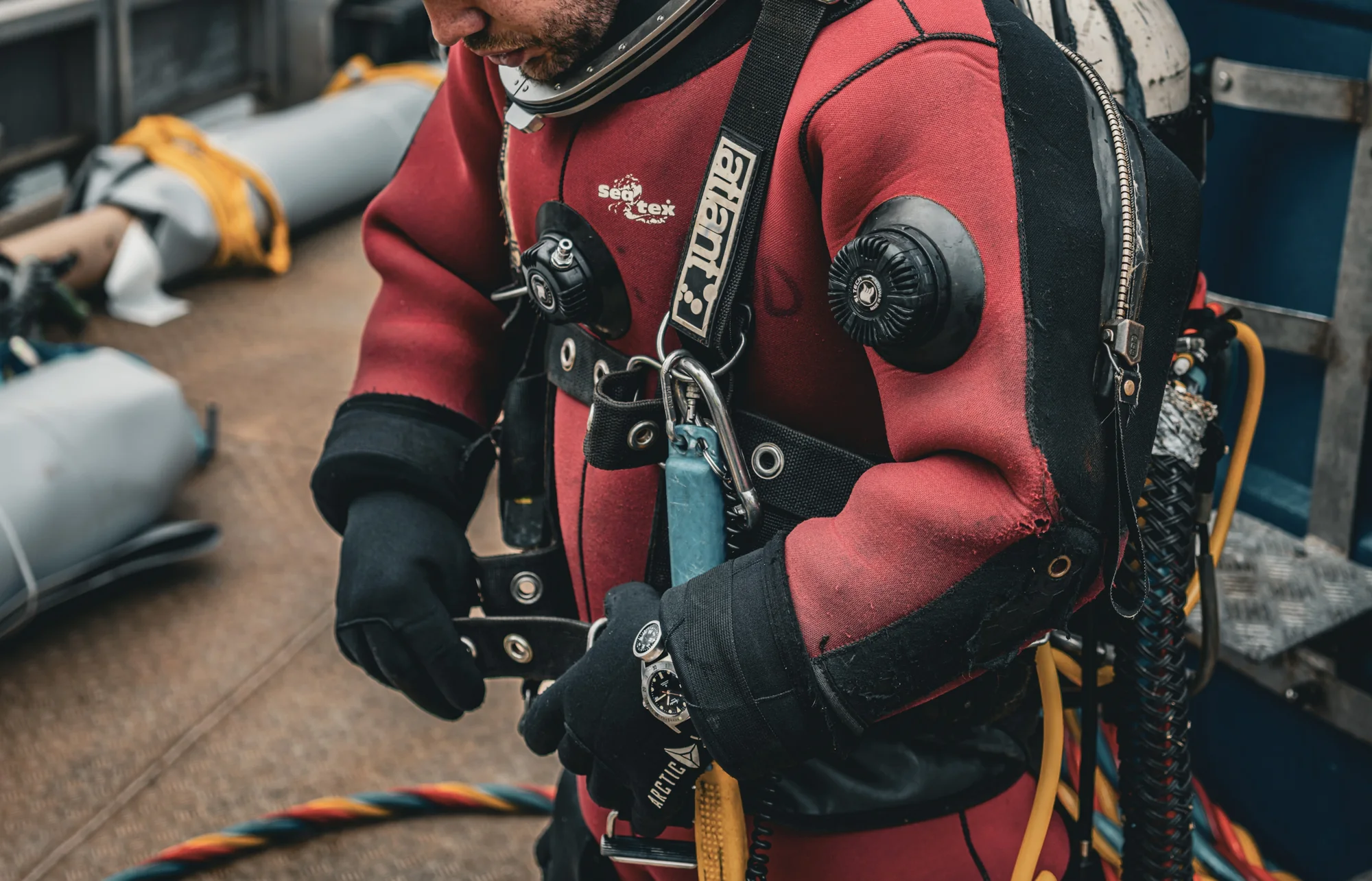 A commercial diver in a red surface-supplied suit wearing an Aquastar Deepstar chronograph on the wrist, aboard a dive support vessel