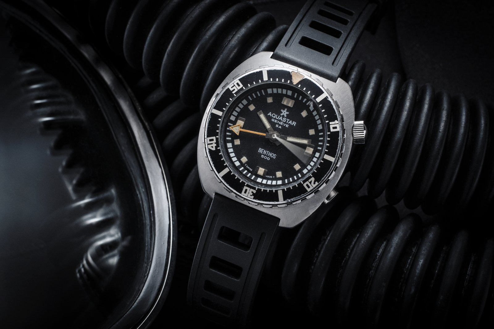 Vintage Aquastar Geneve SA Benthos 500, black dial with tritium lume aged to cream, on black perforated rubber strap next to a corrugated diving regulator hose