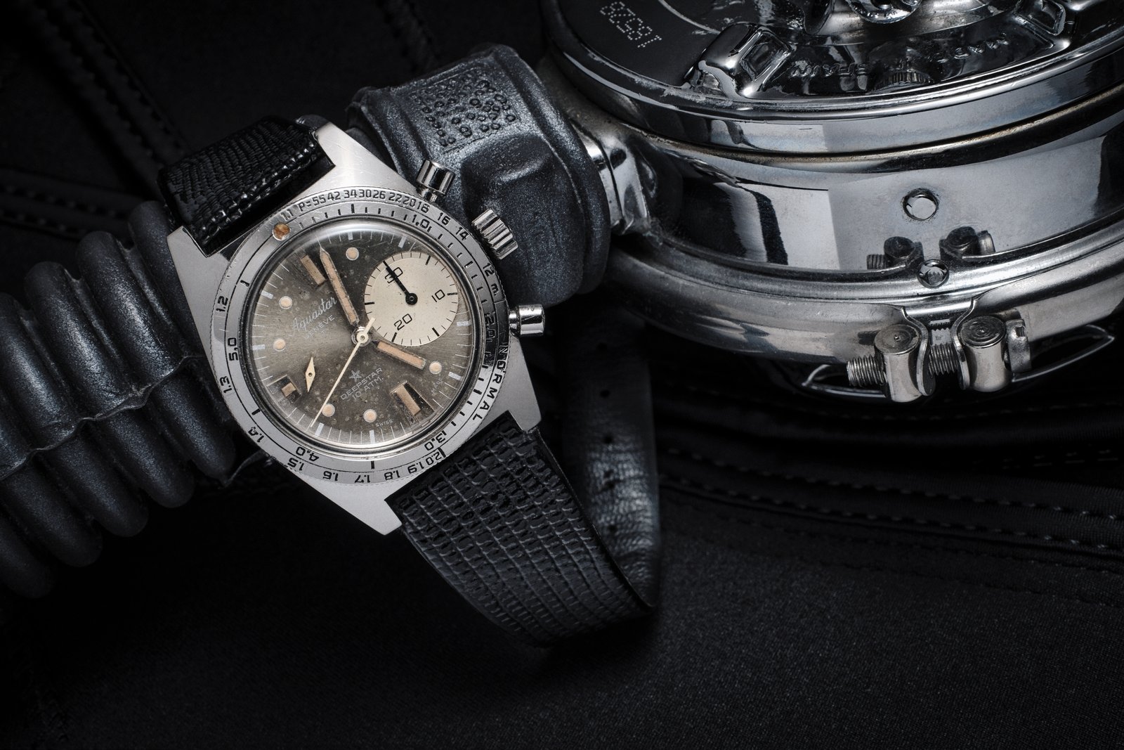 Vintage Aquastar Deepstar 10 ATM chronograph, silver dial with cream-aged tritium markers, on black lizard-grain leather strap, resting on a chromed vintage diving regulator