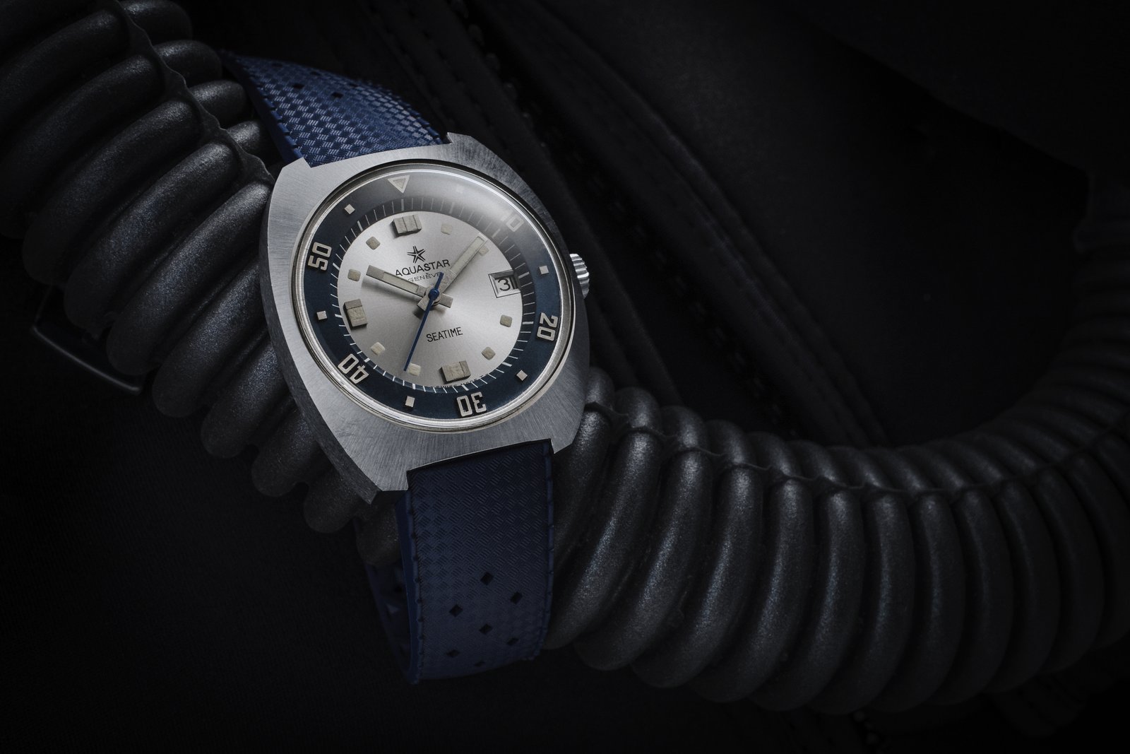 Vintage Aquastar Seatime, silver dial with a deep-blue inner rotating bezel, on a blue TROPIC-style rubber strap resting on a corrugated black diving regulator hose